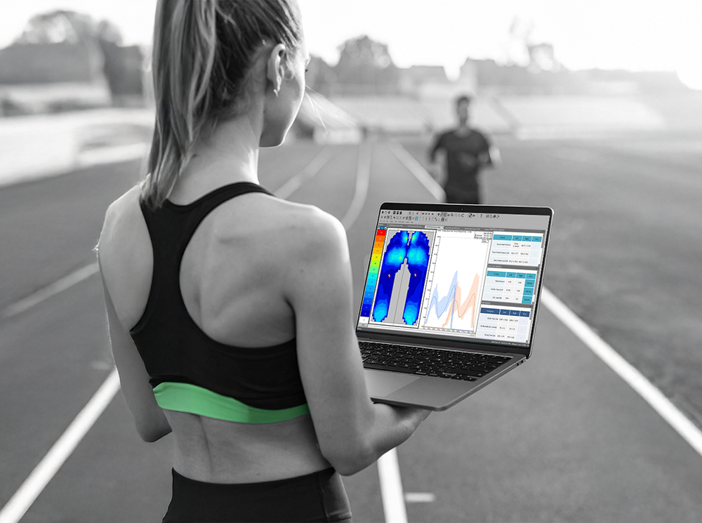 A female coach tracking a runner with a computer using XSENSOR's Intelligent Insoles. A female coach tracking a runner with a computer using XSENSOR's Intelligent Insoles.