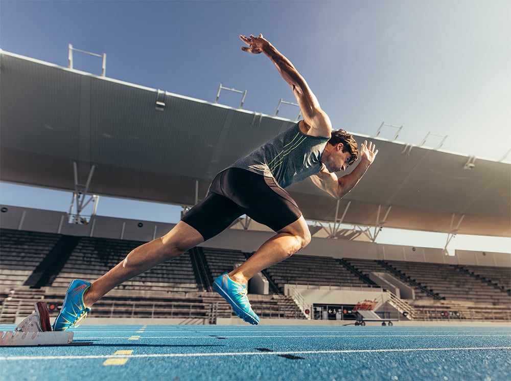 Runner beginning to sprint off of a starting block on a race track.