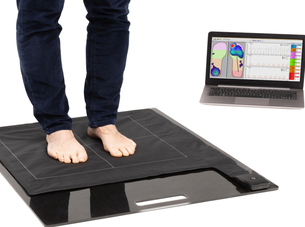 Person standing on XSENSOR's Stance Pad Sensor with their live pressure image on a computer.