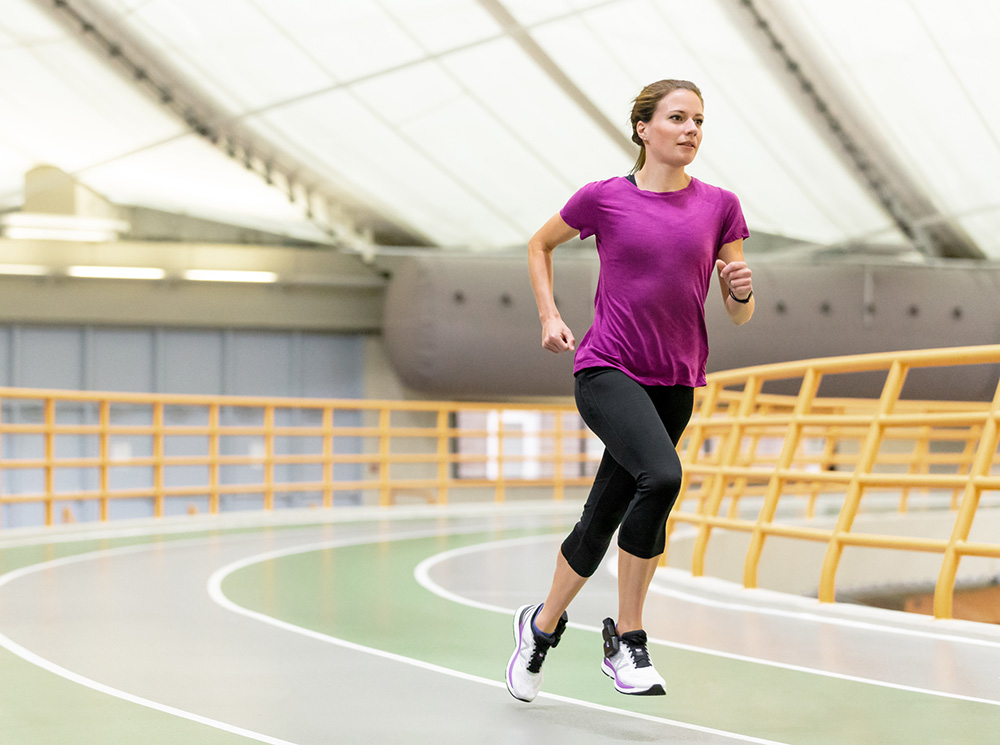 A female athlete is running around a running track with XSENSOR's Intelligent Insoles in her shoes.